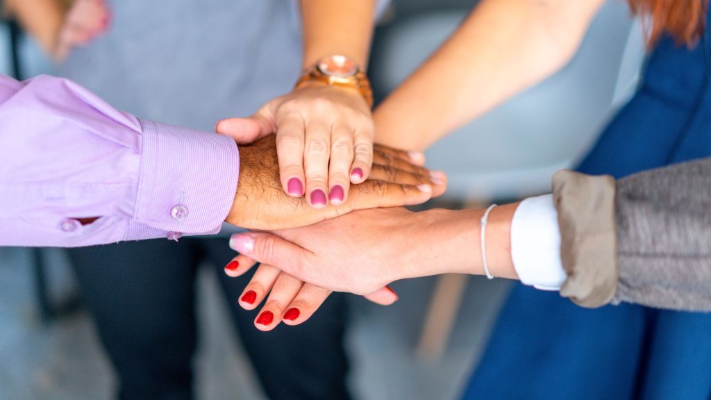 Braccia di persone diverse tese per mettere le mani una sopra l'altra, in segno di sostegno reciproco