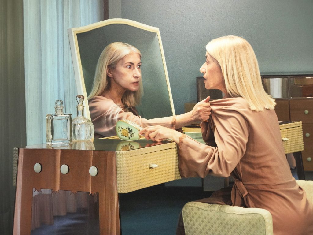 Una donna si sta pettinando allo specchio e la sua immagine riflessa esce dallo specchio afferrandola minacciosamente